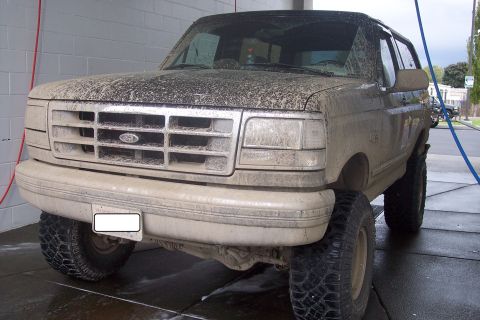 1995 Ford Bronco - This heavily soiled Ford Bronco is positioned for a wash, showing its front end and side profile.