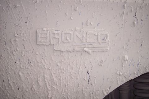 1995 Ford Bronco - Close-up of a Bronco emblem on a textured surface, with a tire visible.