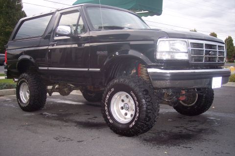 1995 Ford Bronco - This lifted black Ford Bronco is shown from a 3/4 front angle, highlighting its off-road tires and raised suspension.