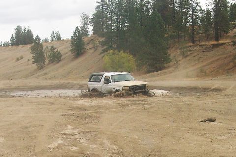 1995 Ford Bronco - White 1995 Ford Bronco navigating a muddy off-road trail.