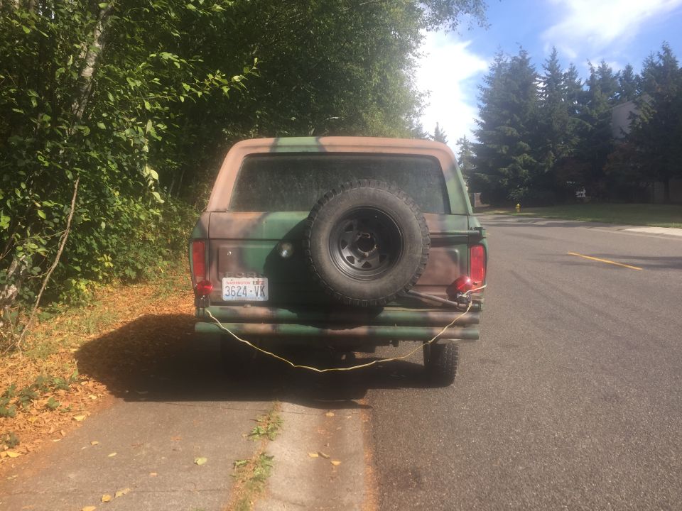 Rear view of a 1978 Ford Bronco in camouflage paint with a spare tire mounted on the tailgate