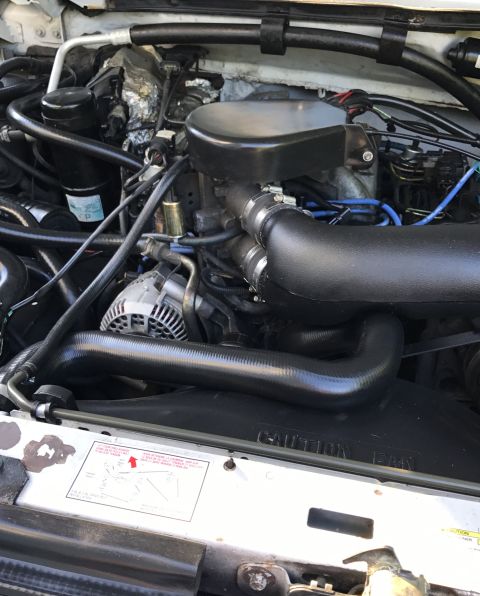 1995 Ford Bronco - Engine bay of a 1995 Ford Bronco, showing the intake system, alternator, and various hoses and wiring.