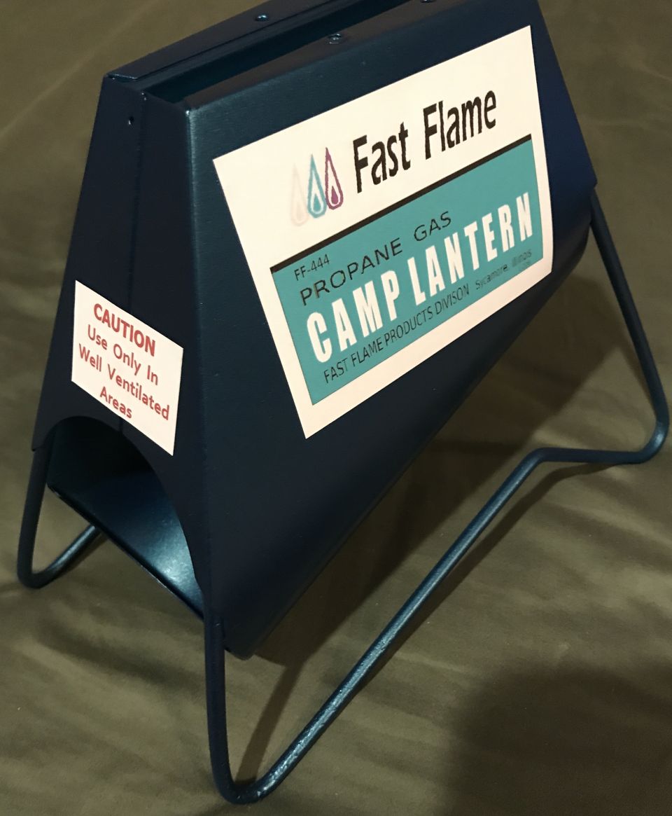 Dark blue metal camp lantern with "Fast Flame" and "CAMP LANTERN" labels, on wire legs