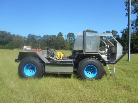 1992 Ford Bronco - This custom-built vehicle features large off-road tires with striking blue rims and a utilitarian metal body.