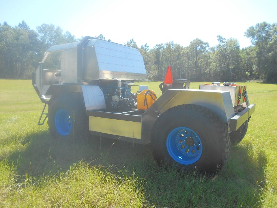 Custom off-road vehicle with large tires and blue rims, parked in a grassy field