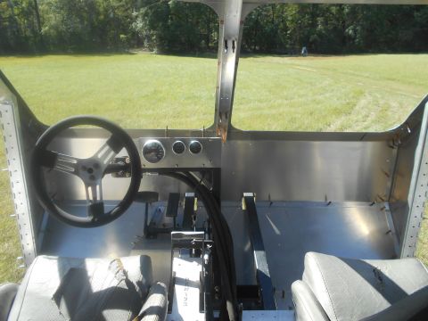 1992 Ford Bronco - The interior of a custom-built vehicle shows a steering wheel, dashboard gauges, and seating, with a grassy field visible through the open…