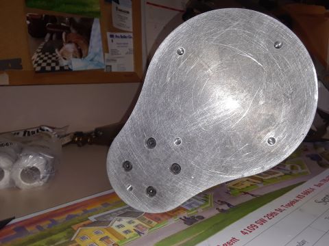 1994 Ford Bronco - A metal component with visible screw holes sits on a surface with printed material and supplies.