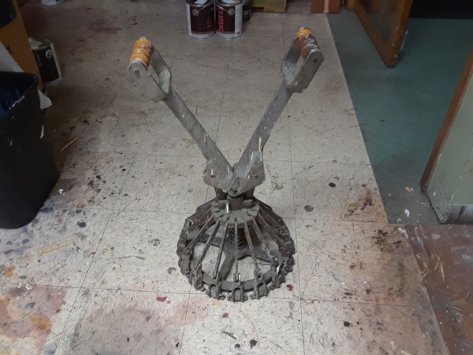 metal tool with two handles and a cage-like bottom, sitting on a dirty floor