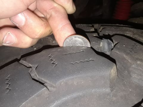 1985 Ford Bronco - A quarter is used to measure the tread depth of a worn and cracked tire.