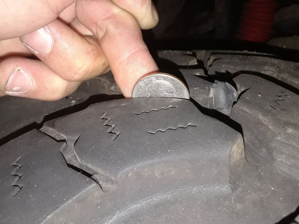 Tire tread with a quarter for scale, showing significant wear and cracking