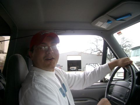1994 Ford Bronco - A man is behind the wheel of a vehicle, with a garage and another truck visible in the background.