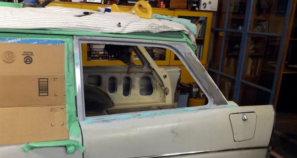Car door frame with tape and primer, showing interior paneling and window opening. Boxes stacked on the left