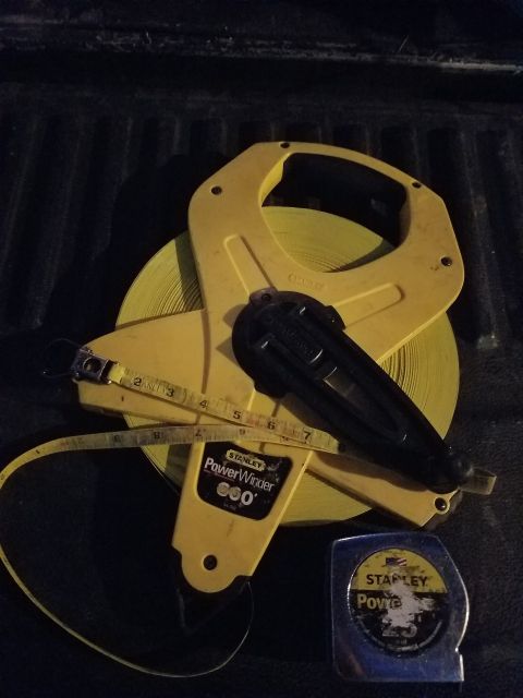1990 Ford Bronco - A yellow Stanley PowerWinder tape measure is shown with a utility knife and a smaller tape measure, likely in the bed of a truck.