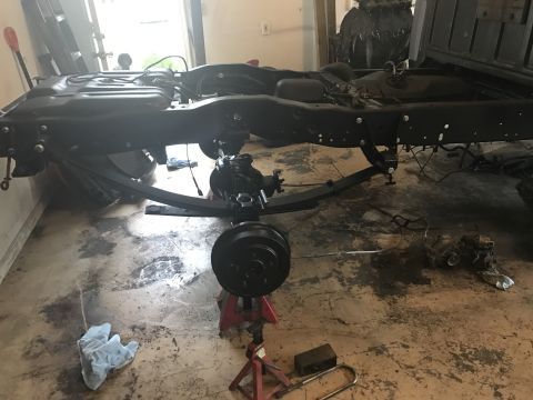1995 Ford F-150 - The rear suspension and frame of a truck are visible, supported by jack stands in a garage.