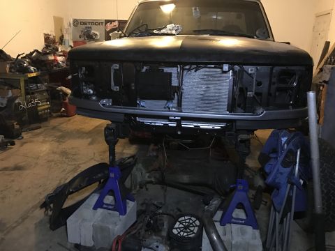 1995 Ford F-150 - The front end of a 1995 Ford F-150 is visible, supported by jack stands in a garage setting with parts scattered around.