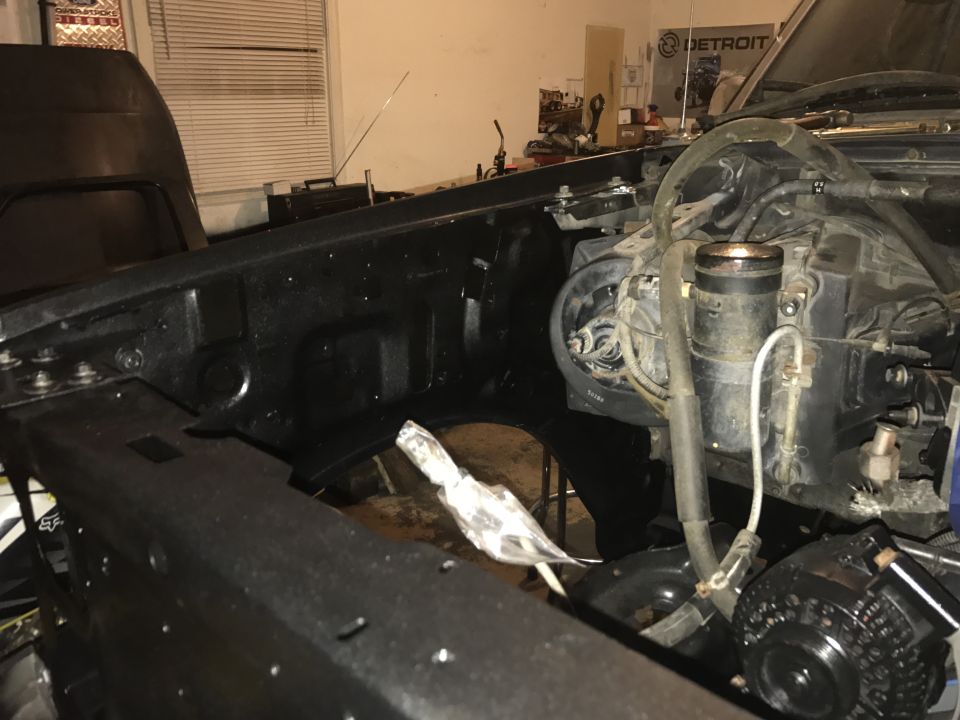 Truck engine bay with hood open, showing engine components and black painted frame. Some wiring and hoses are visible