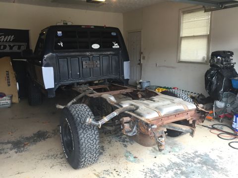 1995 Ford F-150 - The rear section of a black Ford F-150 truck chassis is visible, undergoing repairs in a garage.