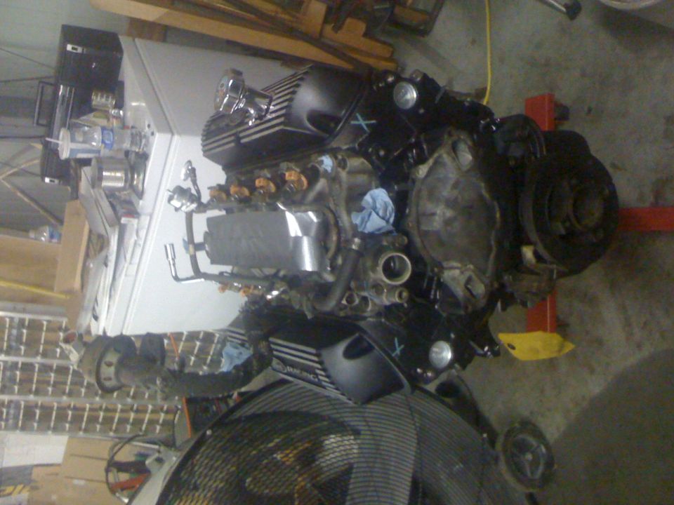 V8 engine assembly on an engine stand, mostly black with silver and chrome parts.