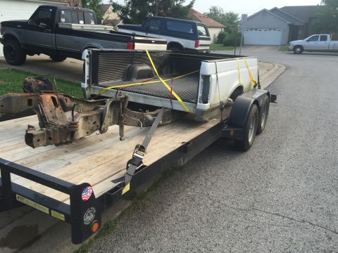 1995 Ford F-150 - A white 1995 Ford F-150 truck bed and chassis are loaded onto a trailer, with other trucks visible in the background.