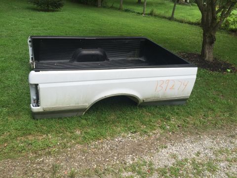 1995 Ford F-150 - A white pickup truck bed is shown from a side angle, resting on grass. Orange handwritten numbers are visible on the side of the bed.