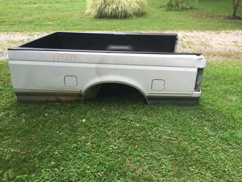 1995 Ford F-150 - A silver pickup truck bed is shown from the side, resting on a grassy lawn. Orange handwritten numbers "139274" are visible on the side of…