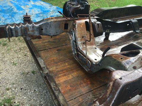 1995 Ford F-150 - A rusty, wet vehicle frame is resting on a wooden trailer. The frame appears to be from an older truck, possibly a Ford F-150, with some vi…