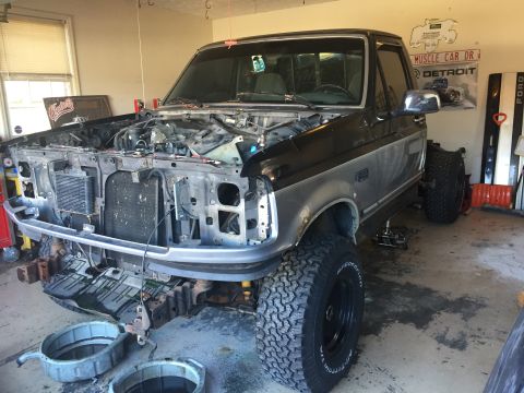 1995 Ford F-150 - A black and silver Ford F-150 pickup truck is parked in a garage with its hood removed, undergoing mechanical work. The front end is disass…