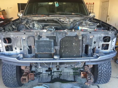 1995 Ford F-150 - The front end of a dark-colored pickup truck is shown with the hood open and the grille removed, exposing the radiator and transmission coo…