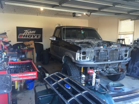 1995 Ford F-150 - A black and silver pickup truck is parked in a garage with its hood removed, undergoing repairs. Various tools and automotive parts are sca…