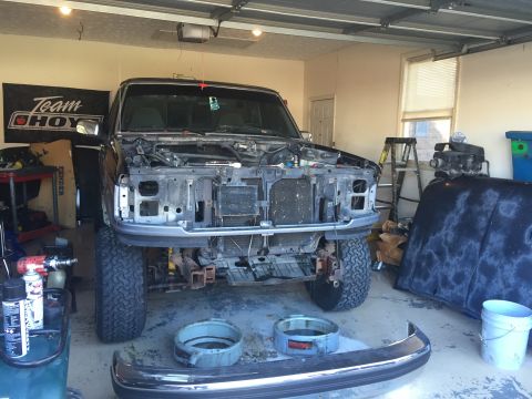 1995 Ford F-150 - A black Ford F-150 pickup truck is parked in a garage with its hood removed, revealing the engine bay. Various car parts, including a bumpe…