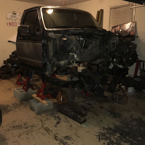 1995 Ford F-150 - A dark-colored pickup truck body is elevated on jack stands in a garage, with the engine and front chassis components removed and disassemb…
