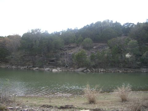1994 Ford Bronco - A tranquil scene of a lake bordered by a rocky, wooded hillside, with dry grass in the foreground.