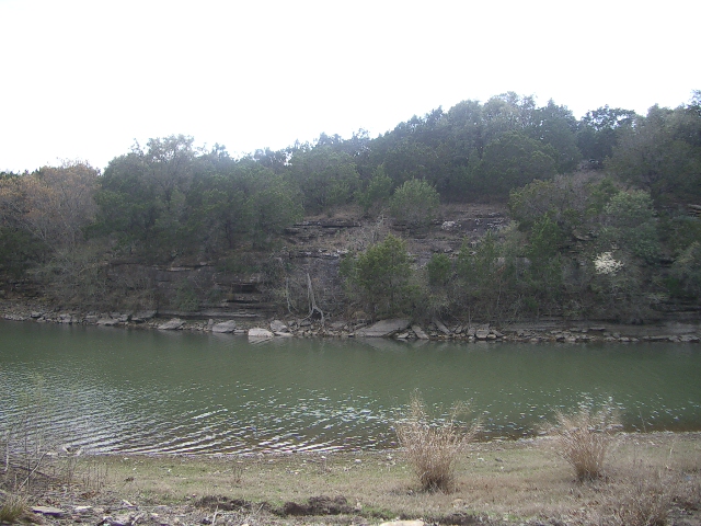 Lake with rippling water and a rocky, tree-covered bank under a hazy sky