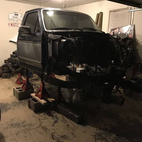 1995 Ford F-150 - A dark blue and silver pickup truck is undergoing a restoration in a garage. The truck is elevated on jack stands, with the engine and fron…