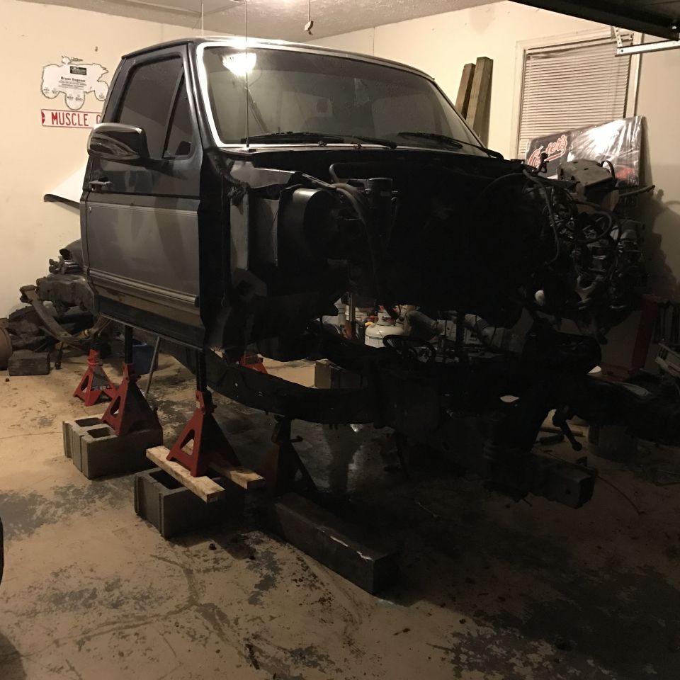 1995 Ford F-150 pickup truck disassembled on jack stands in a garage.
