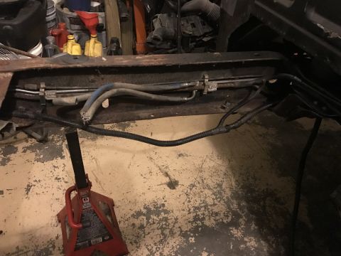 1995 Ford F-150 - A close-up view of the undercarriage of a vehicle, showing fuel lines and wiring harnesses supported by a red jack stand. The scene appears…
