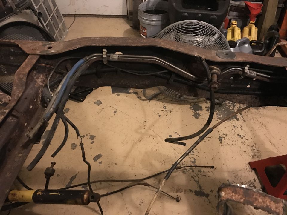 Rusty vehicle frame with hoses and wires, industrial fan in background.