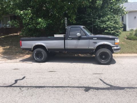 1995 Ford F-150 - A lifted, two-tone black and silver Ford F-150 pickup truck is parked on a residential street. The truck has aftermarket wheels and tires,…