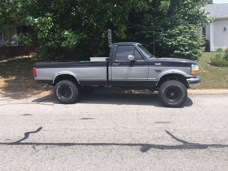 1995 Ford F-150 pickup truck, lifted, two-tone black and silver, parked on street.