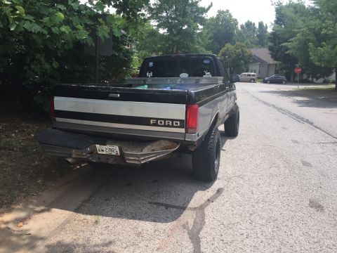 1995 Ford F-150 - The rear driver side of a lifted, black and silver Ford pickup truck parked on the side of a residential street. The truck has large tires…