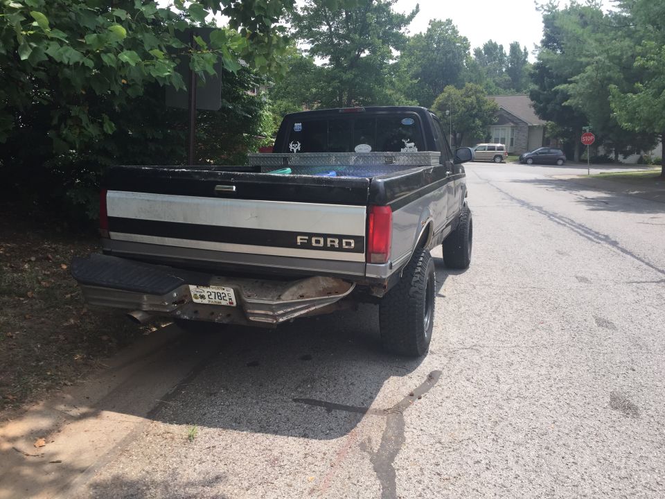 Lifted black and silver Ford pickup truck, rear driver side view, parked on street.