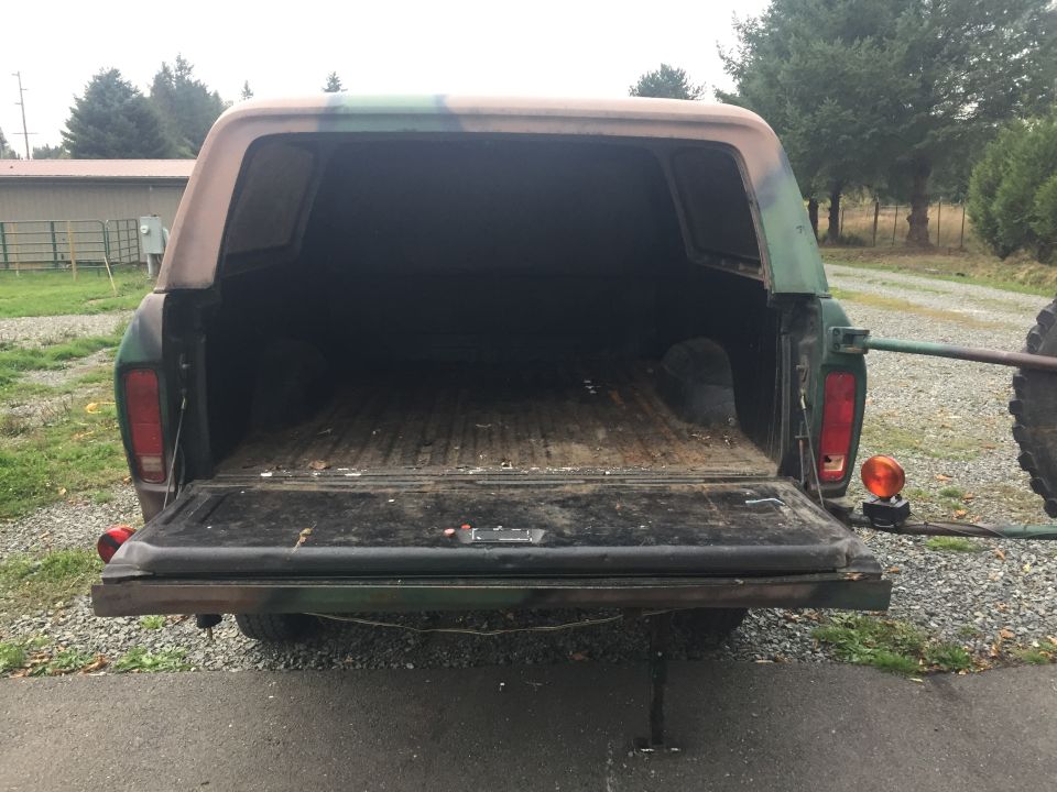 Rear view of a pickup truck with a camouflage camper shell, tailgate down.