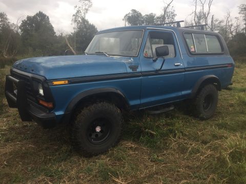 1979 Ford Bronco - This blue SUV is parked outdoors on a grassy area with trees in the background.