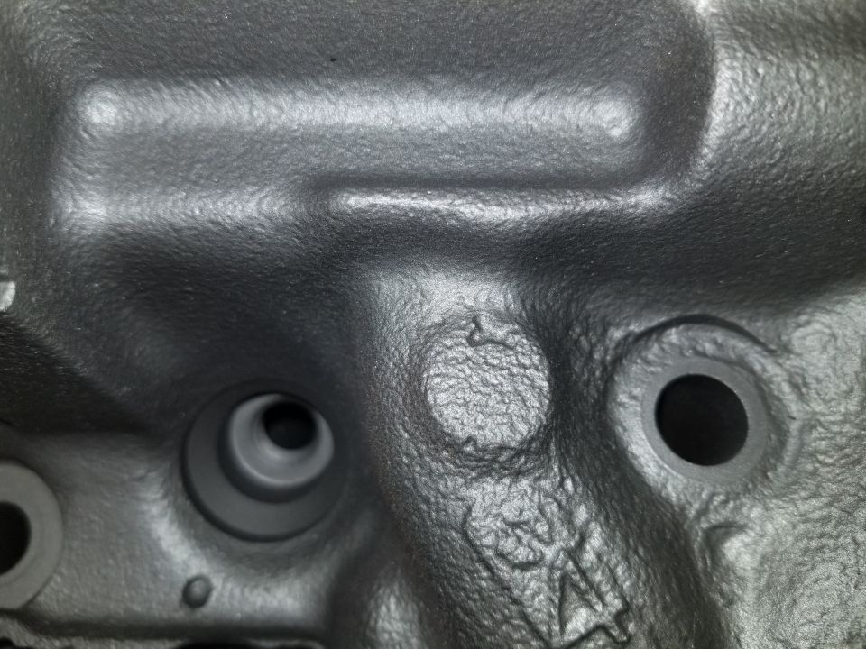 Close-up of a dark gray engine block with circular openings and casting marks.