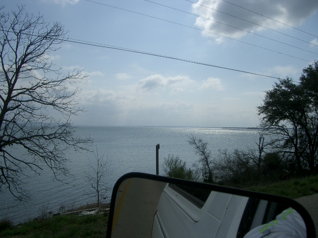 White vehicle side mirror reflection showing part of the vehicle body and a large body of water