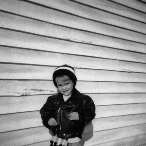 1989 Ford Bronco - A young child wearing a beanie and a leather jacket stands in front of a wood-paneled wall, holding what appear to be toy binoculars.