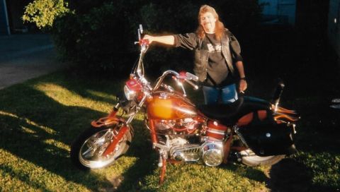 1989 Ford Bronco - A man with a mullet stands next to a custom red and orange motorcycle with flame decals. The motorcycle has chrome accents and black saddle…