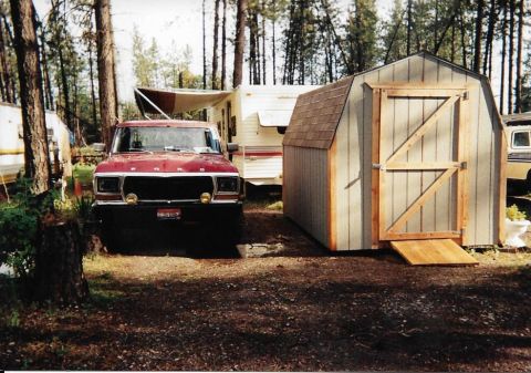 1989 Ford Bronco - A red Ford pickup truck is parked next to a shed at a campsite. A travel trailer is visible behind the truck.