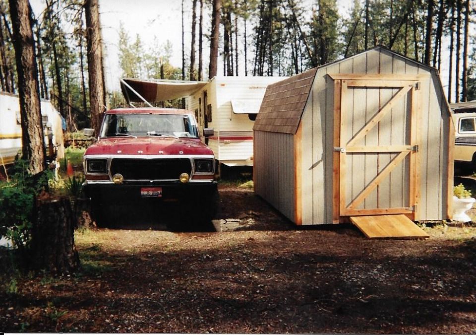Red Ford pickup truck parked next to a shed with a travel trailer in the background.