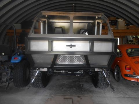1992 Ford Bronco - The rear view of a custom-built, unfinished vehicle with a metal frame and body panels is shown inside a garage. An orange Volkswagen Beetl…